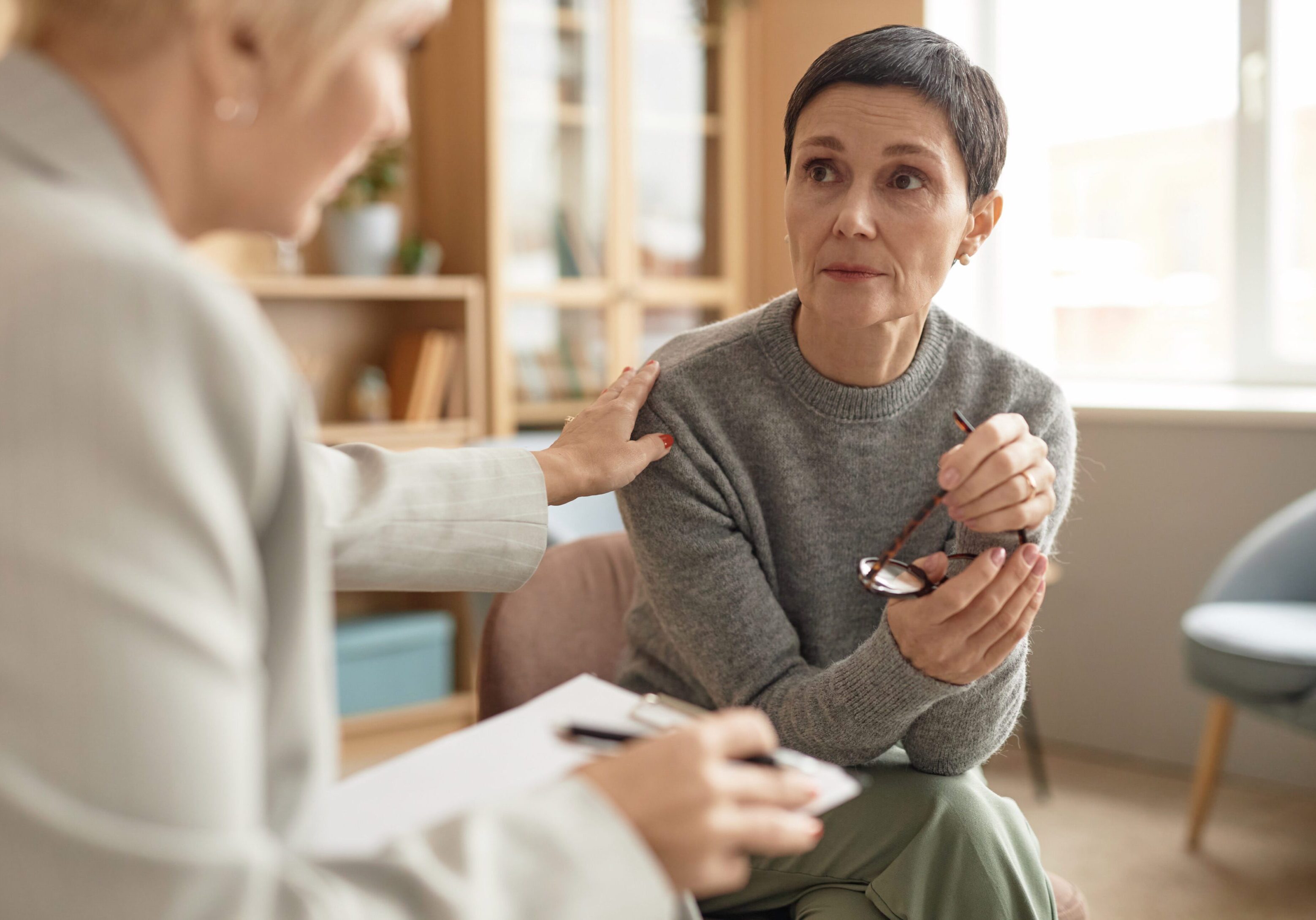 Distressed Mature Woman Listening to Female Psychologist A woman sitting on the floor with another person.